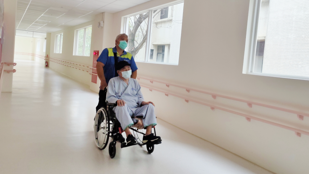 在台中榮民總醫院嘉義分院擔任傳送的小汪推著輪椅的病人去做檢查