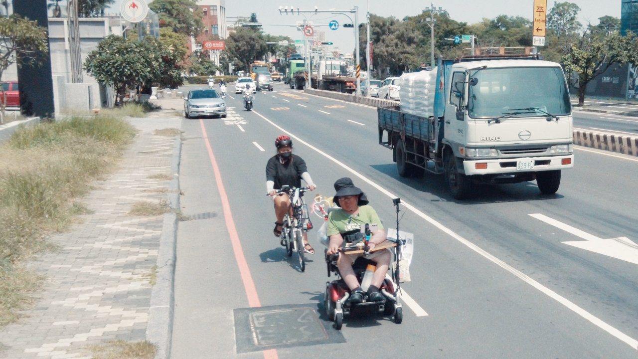 人行道長滿了雜草，不方便輪椅行走，小齊只能冒險走到馬路上，與車同行